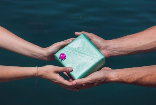close-up-couple-s-hand-holding-gift-box-front-sea_23-2147887895